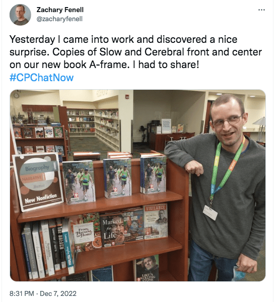 an image of zach posting in front of copies of his book at his library